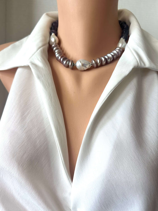 A close-up of a beaded necklace displayed on a mannequin torso wearing a white collared blouse. The necklace features a mix of dark PURPLE cord, silver-toned beads, and a prominent white pearl-like bead at the center.