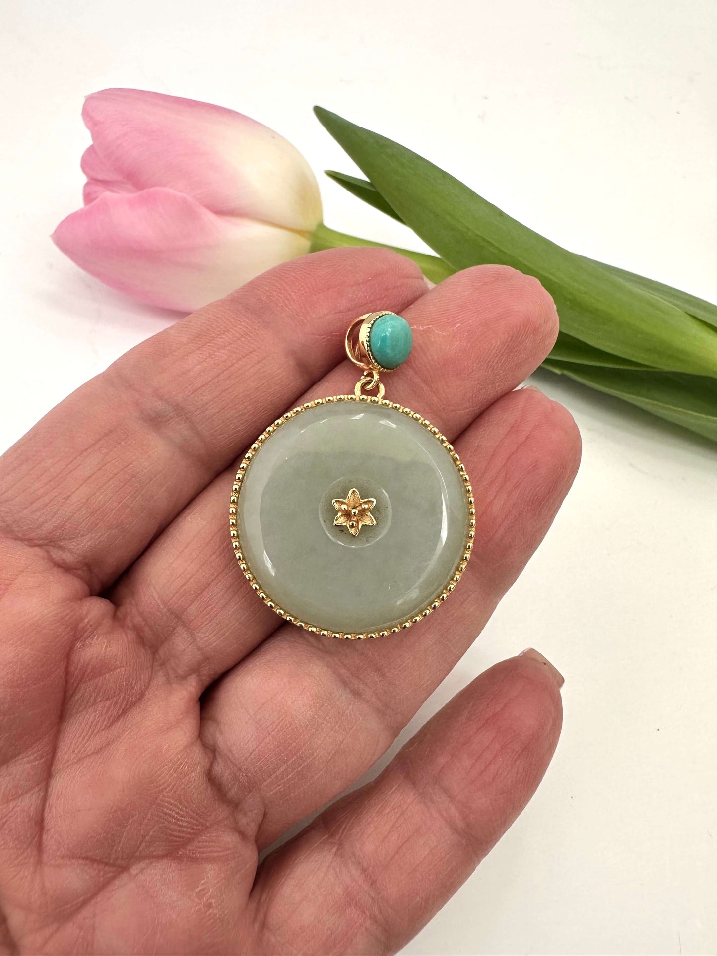 hotan jade pendant with turquoise accent in gold vermeil held in hand with a pink tulip in the background.
