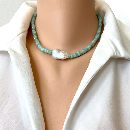 A close-up of a beaded necklace with light blue-green round beads and a large irregular white pearl pendant, worn on a mannequin or model torso in a white collared blouse.