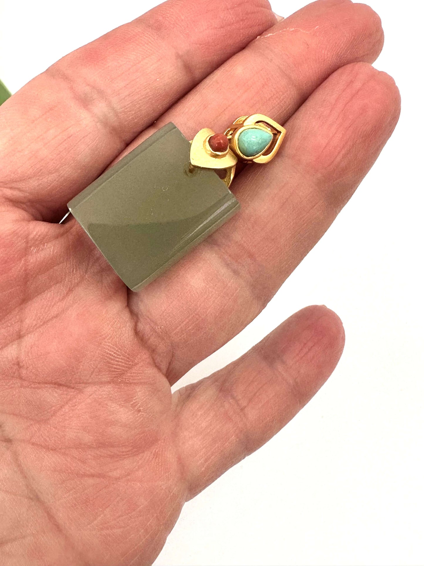 Hotan jade pendant with turquoise and red agate in gold vermeil design held in a hand.