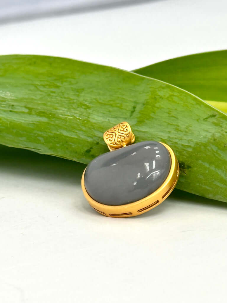 Hotan jade charm pendant in gold bezel resting on a green leaf, featuring a smooth nephrite jade teardrop.
