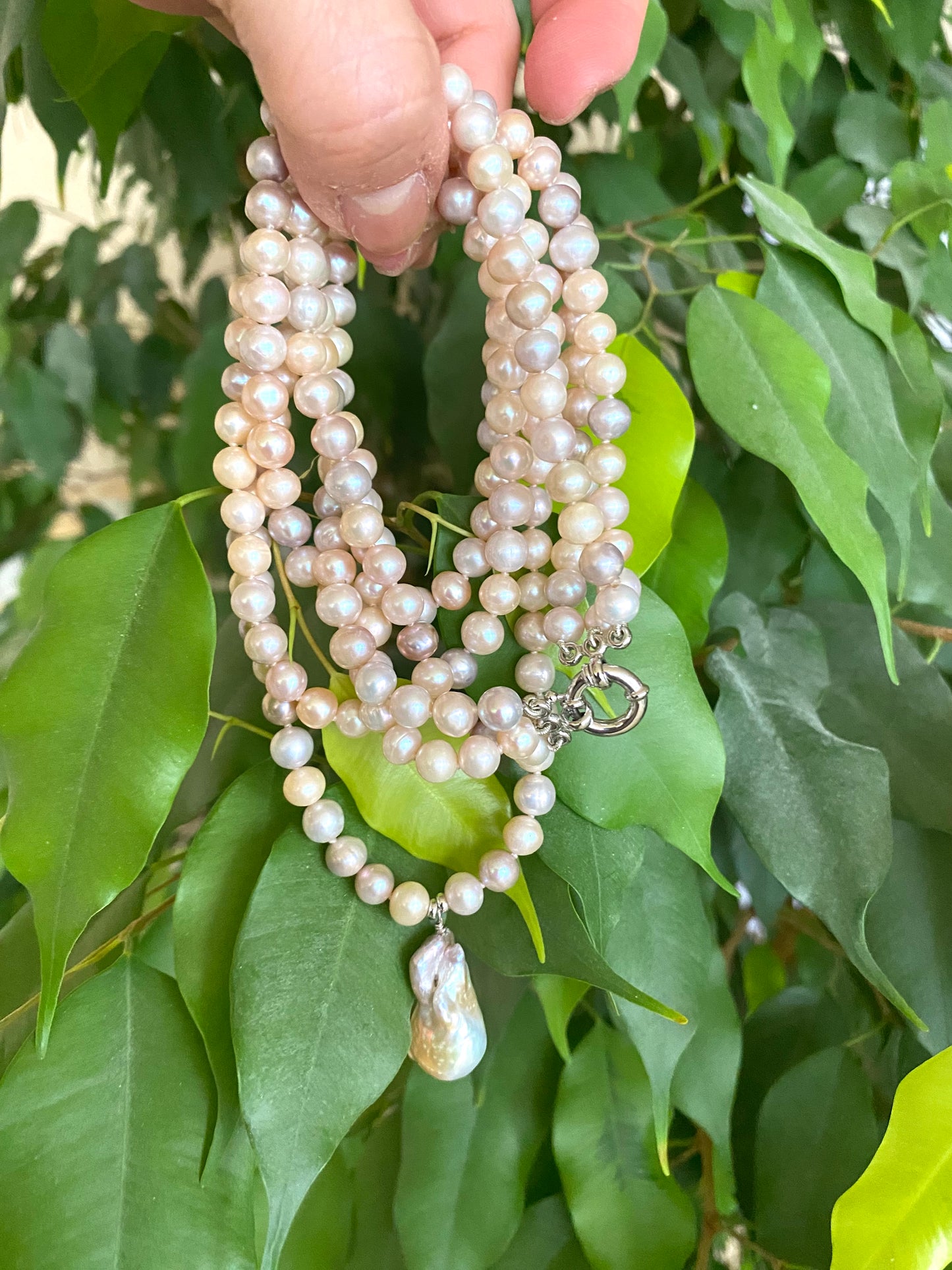 Multiple strands of pearls held against a green leafy background