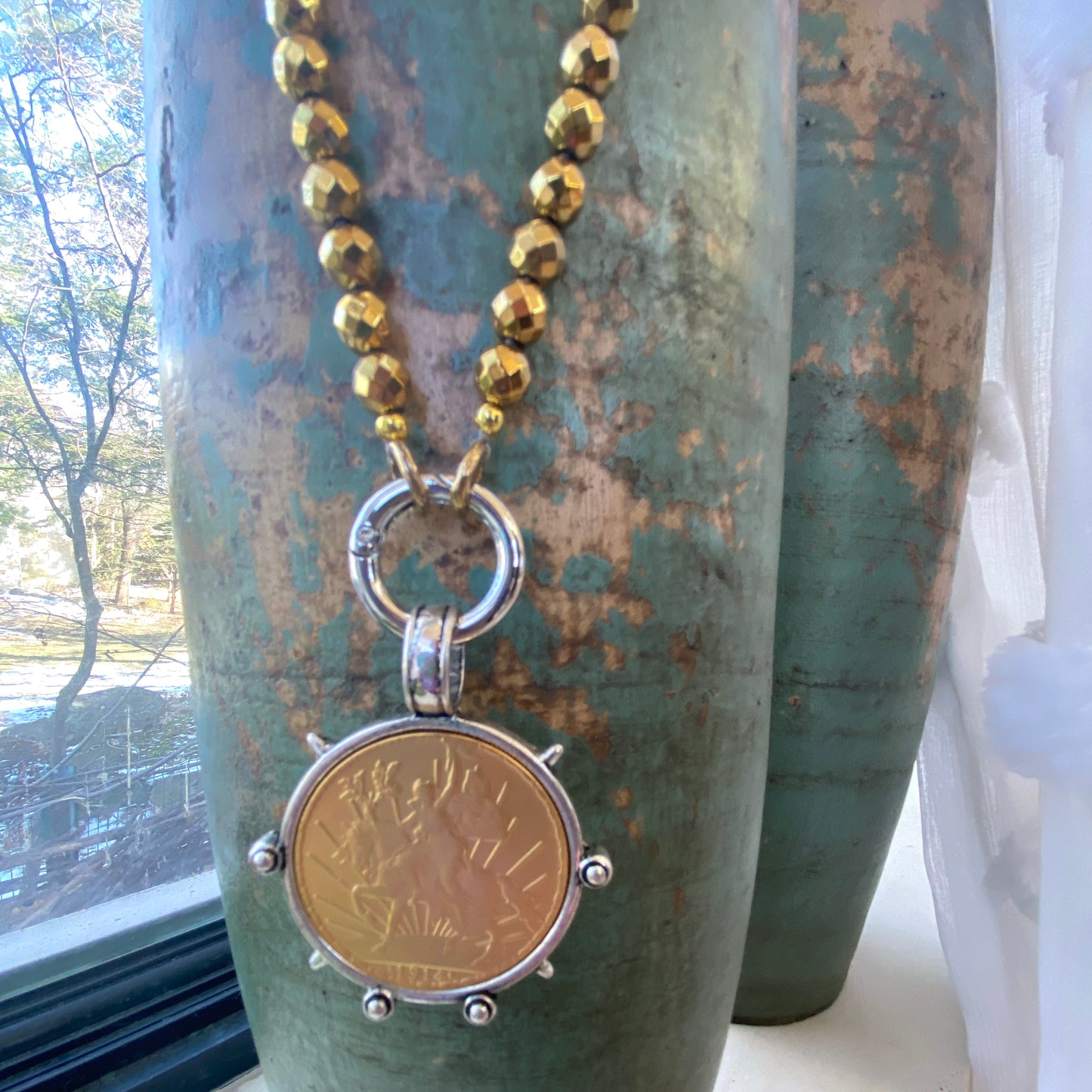 Mexican Peso Coin Pendant Necklace with gold-coated hematite beads displayed near a decorative vase.