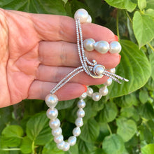 Cargar imagen en el visor de la galería, Natural white baroque pearl necklace with CZ pavé accent, close-up on leafy green backdrop.
