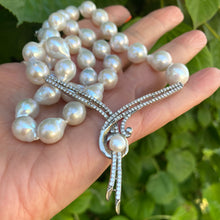 Cargar imagen en el visor de la galería, Baroque pearl necklace with sterling silver clasp held in hand against green leaf backdrop, close-up view.