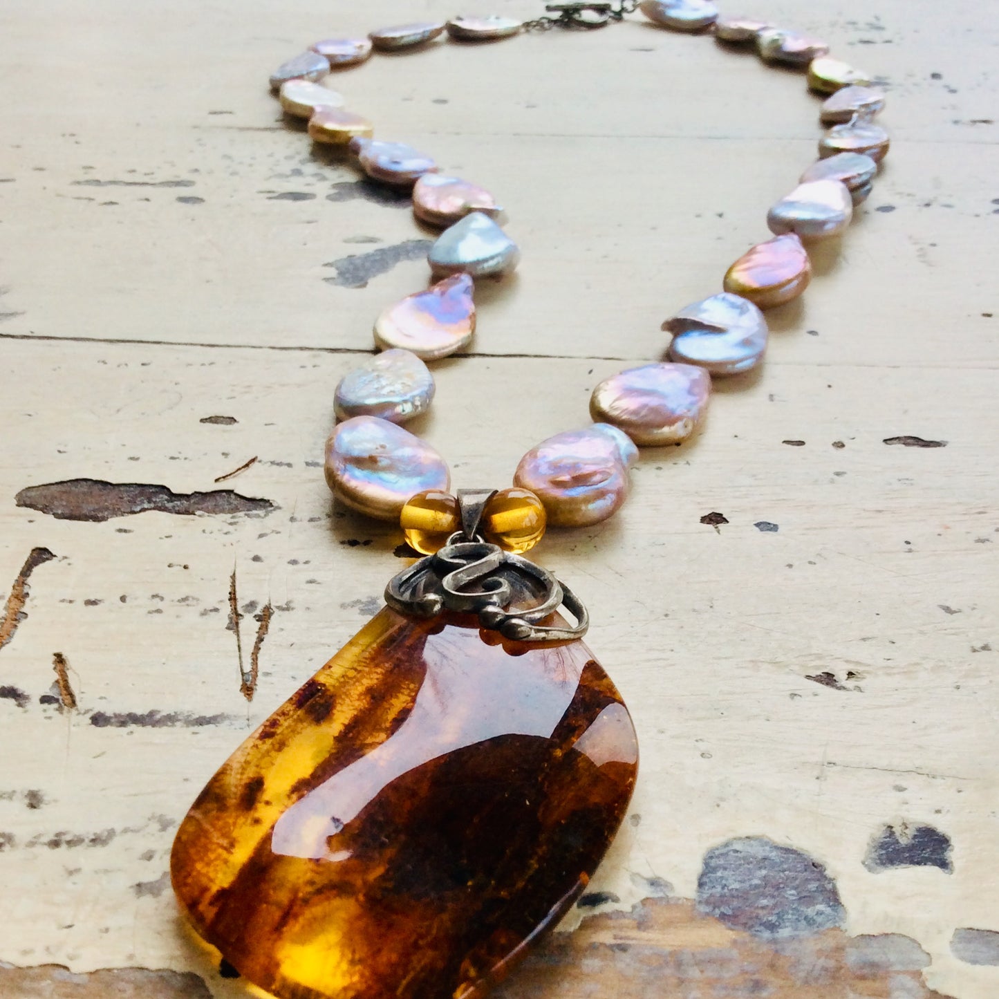 Handcrafted keshi pearl necklace with sterling silver amber pendant on white wood surface.