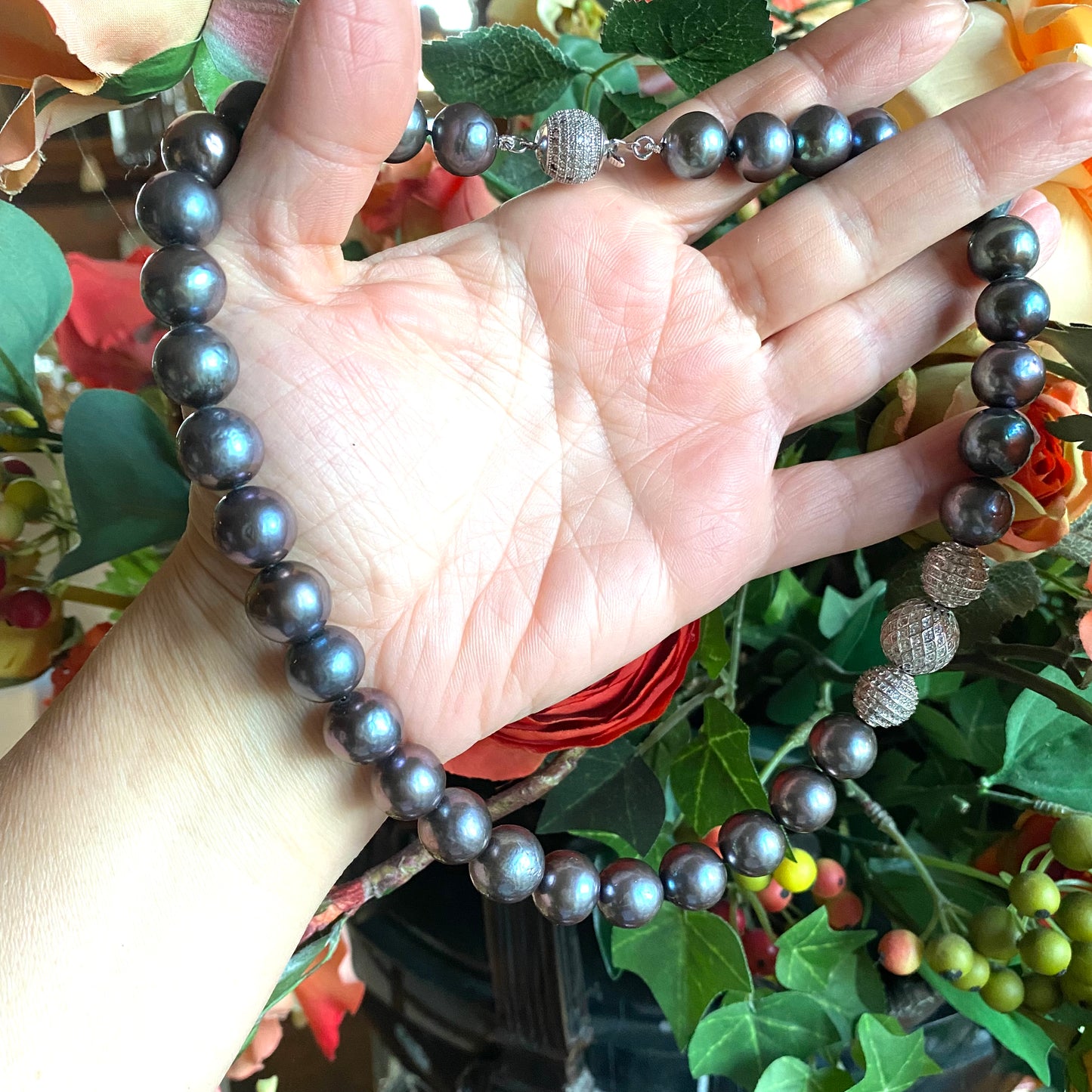 Handcrafted black pearl silver necklace in natural light, held by woman’s hand with mistletoe and green foliage