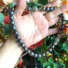 Carica l'immagine nel visualizzatore di Gallery, Handcrafted black pearl silver necklace in natural light, held by woman’s hand with mistletoe and green foliage