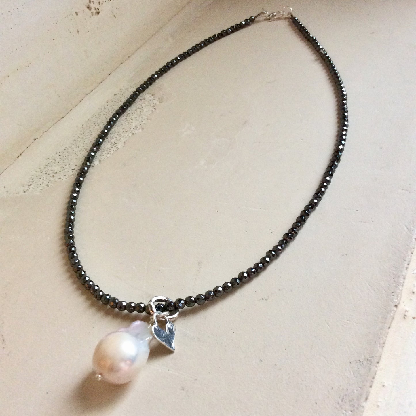Hematite necklace with baroque pearl pendant displayed flat emphasizing minimalist design