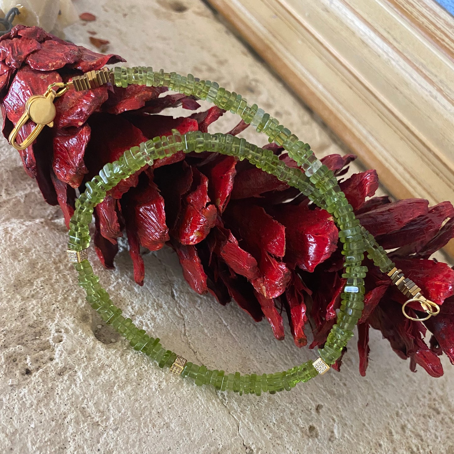 Peridot choker necklace with natural green peridot beads displayed elegantly against red floral background.