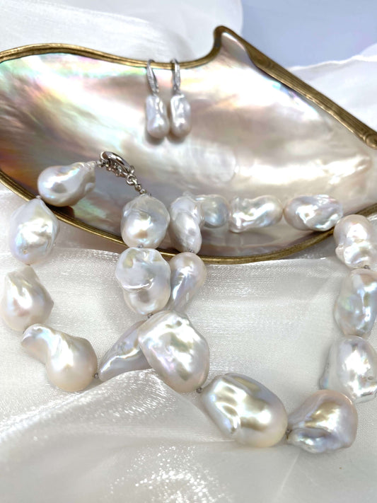 Handcrafted baroque pearl necklace and drop earrings displayed on an iridescent shell, showcasing bridal design jewelry by Loulia Pearl Jewelry