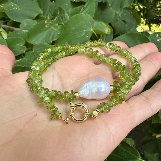 Gold peridot necklace with pearl centerpiece held in hand against green foliage