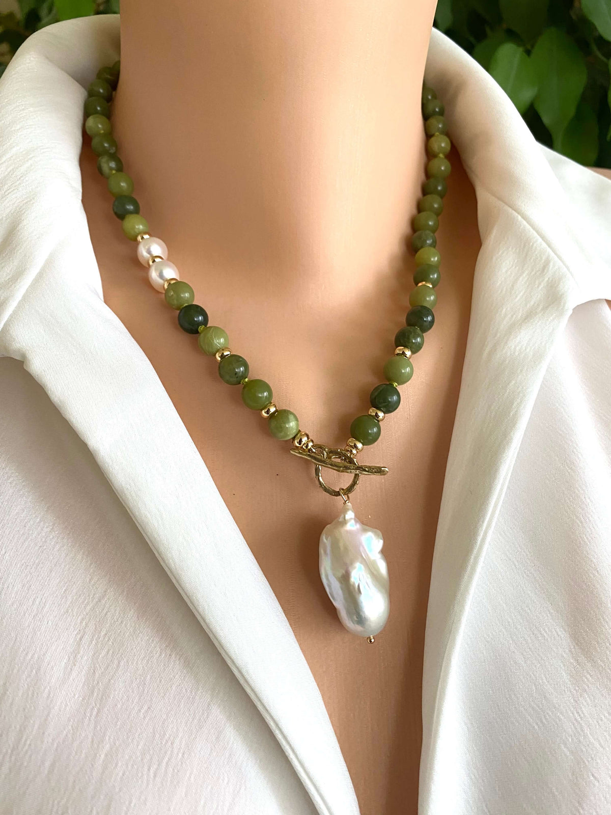 Necklace with green beads and a large white pearl on a mannequin wearing a white shirt.