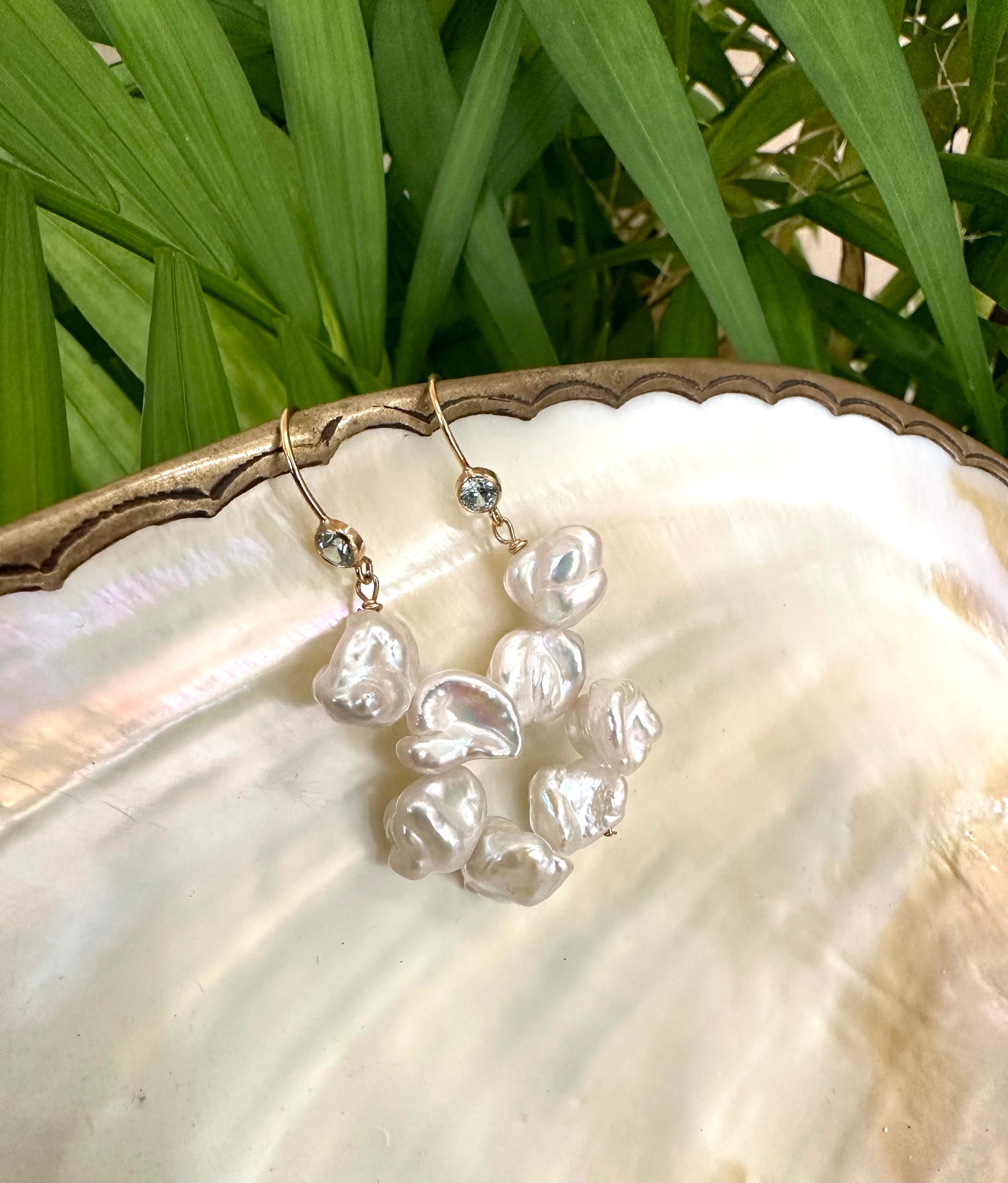 Pearl drop earrings featuring keshi pearls and blue CZ, elegantly displayed on a seashell with greenery.