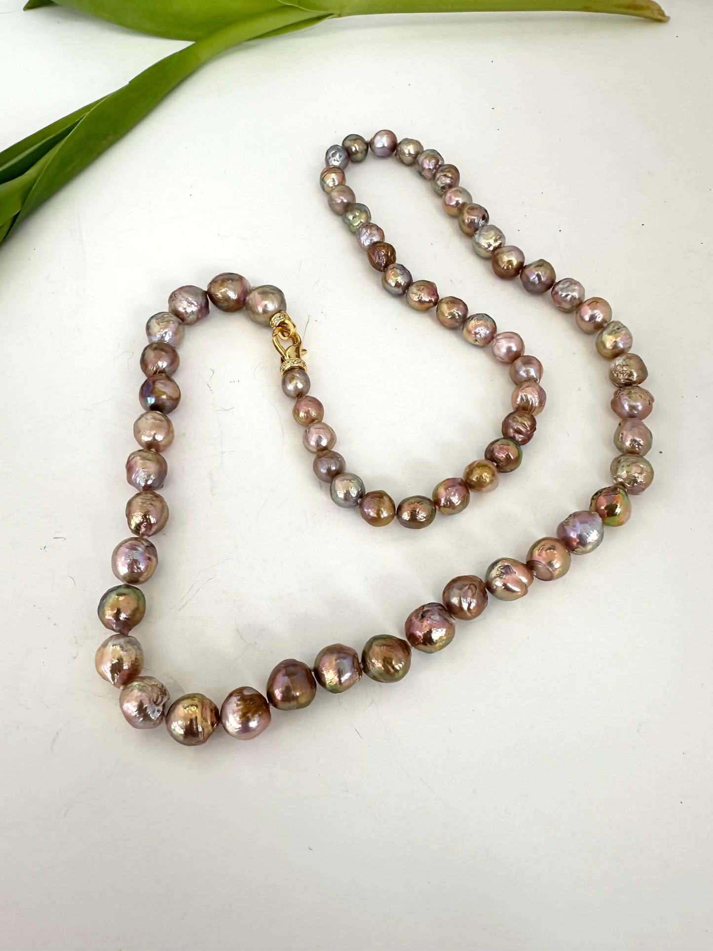Pearl necklace on a white surface with green leaves in the background