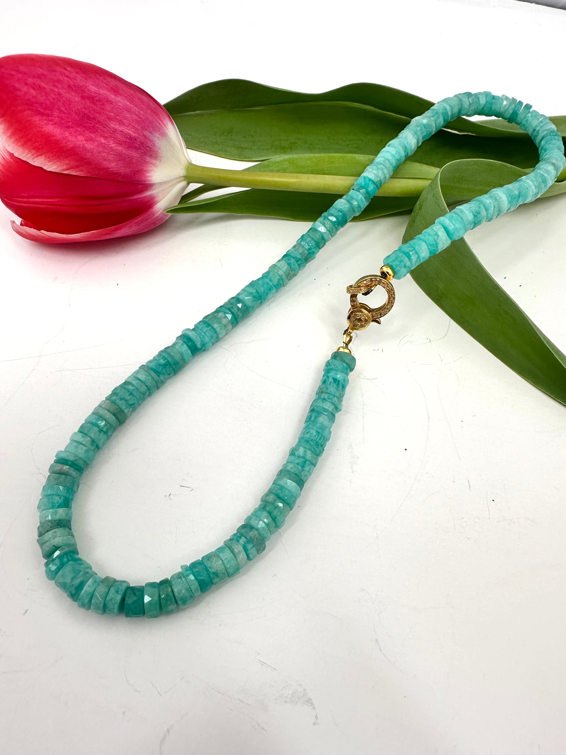 AMAZONITE beaded necklace with a gold clasp on a white surface with a pink tulip and green leaves.