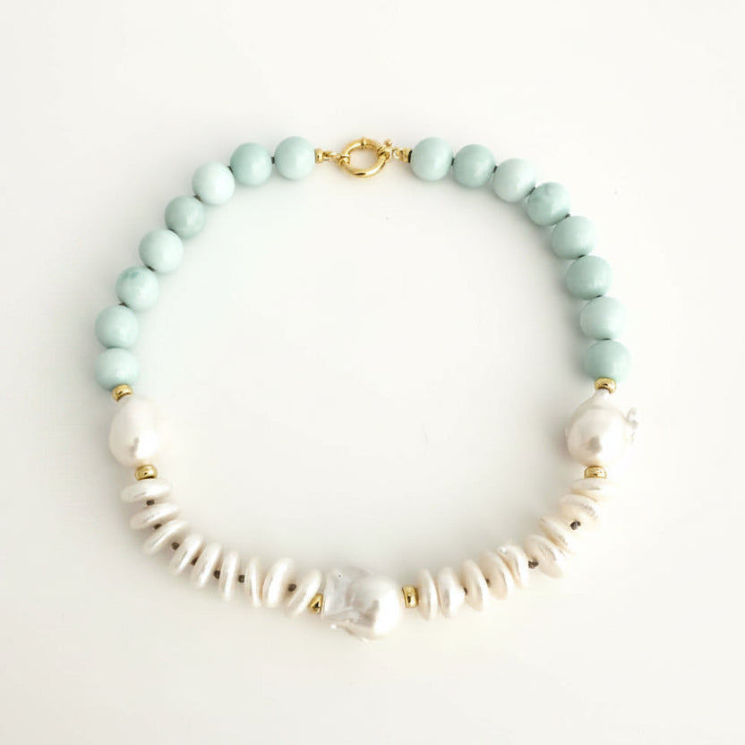 light amazonite green faceted round beads, white baroque pearls, and textured white coin pearls, accented with small gold spacers and a gold clasp, displayed on a light off-white background.