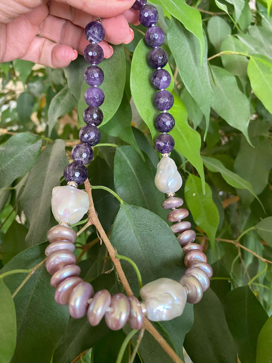 Amethyst pearl necklace with baroque and coin pearls showcasing deep purple and white pearls against green foliage.