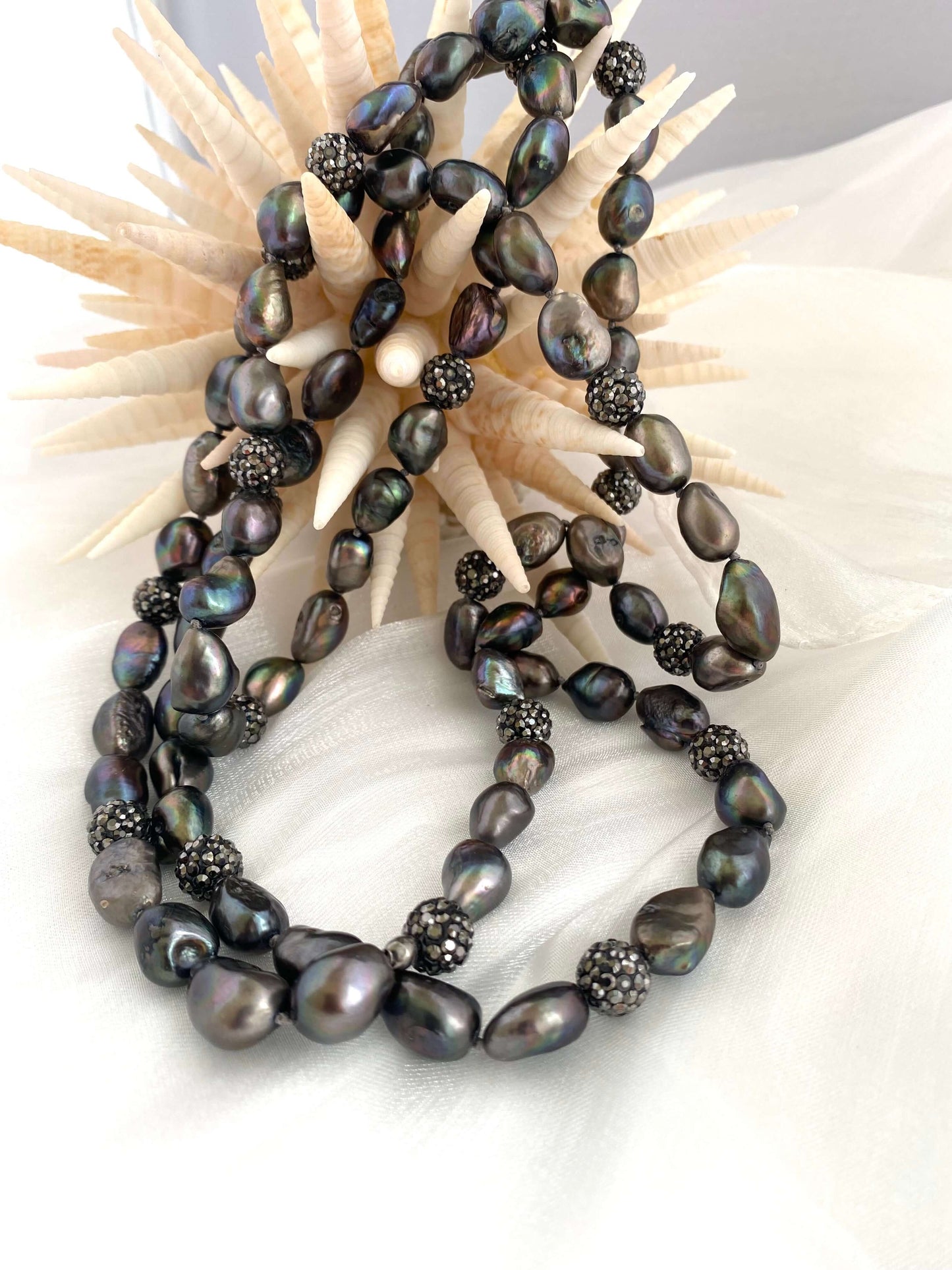 Black pearl necklace on a textured surface with a shell background