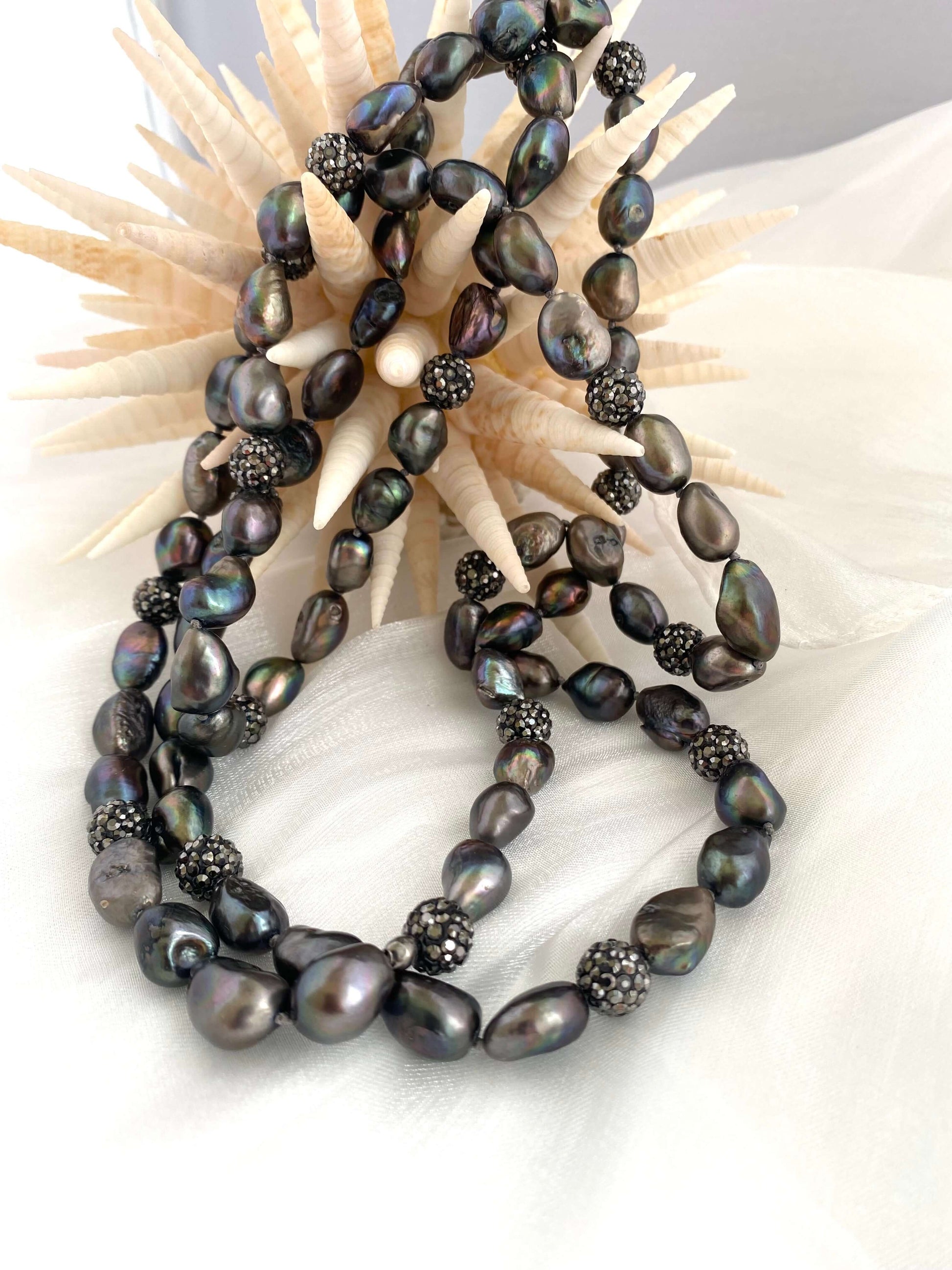 Black pearl necklace on a textured surface with a shell background