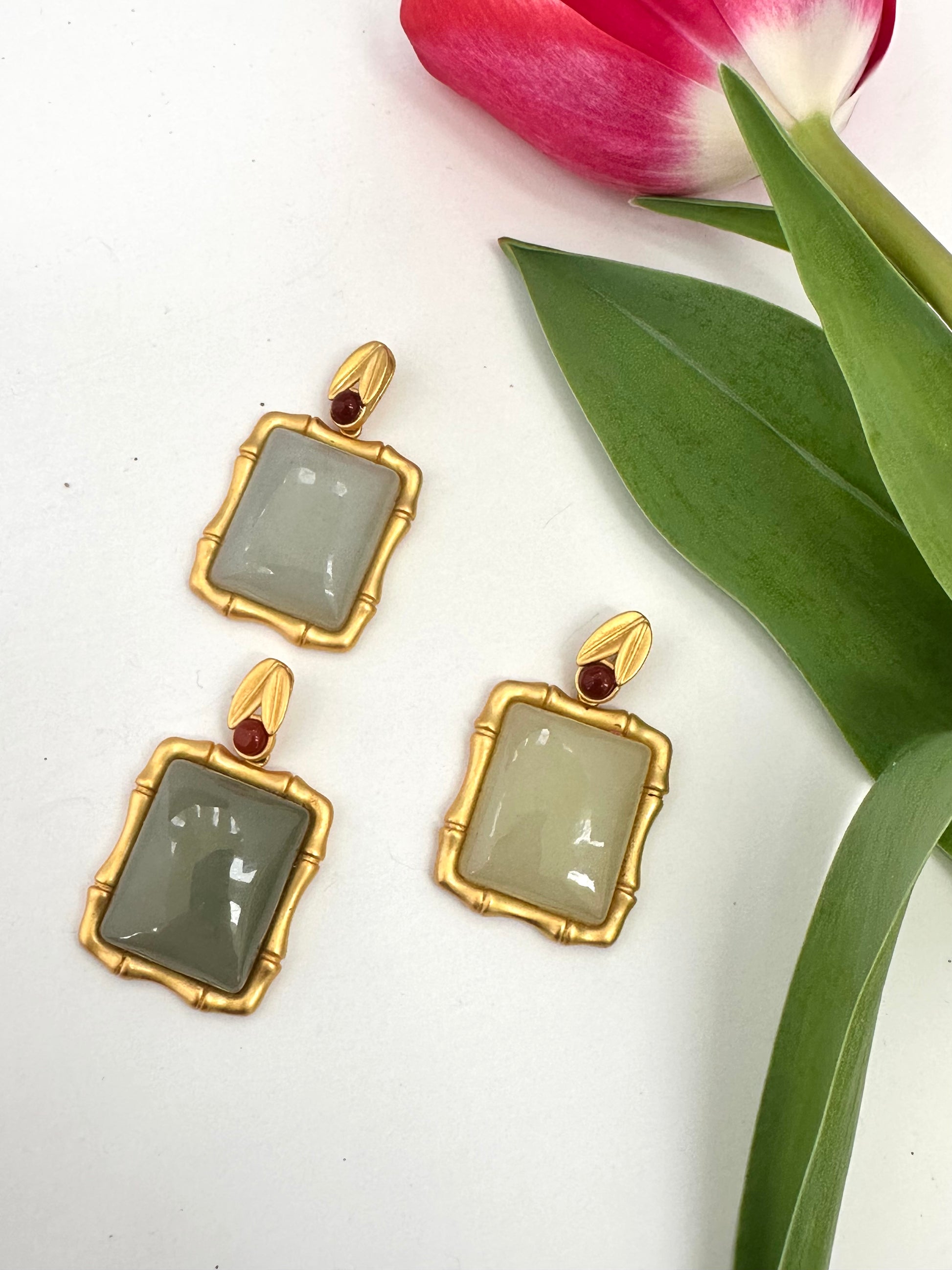 Gold-framed pendants with green stones on a white background with tulip leaves.