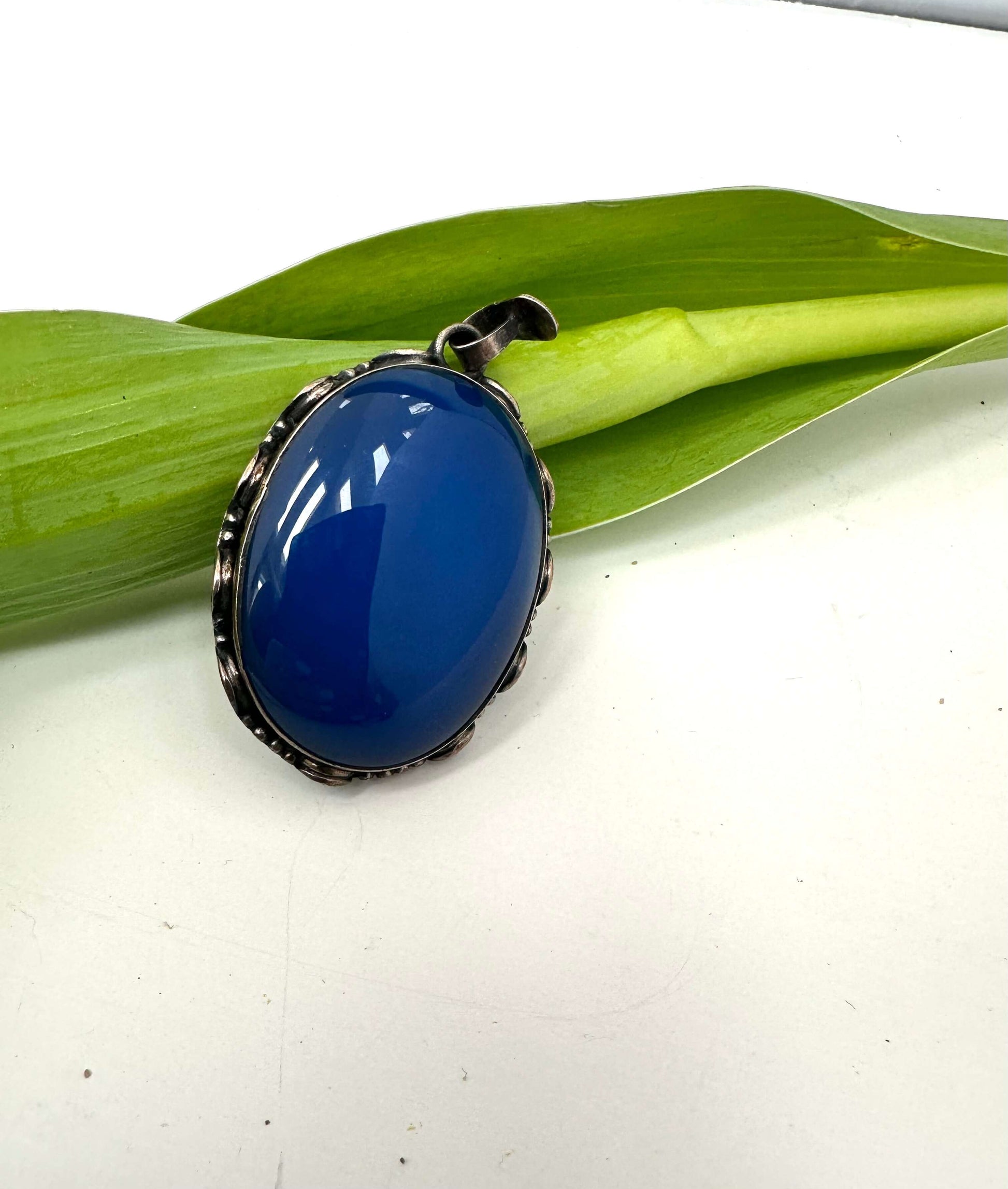 Vintage blue agate pendant in oxidized sterling silver resting on a green leaf.