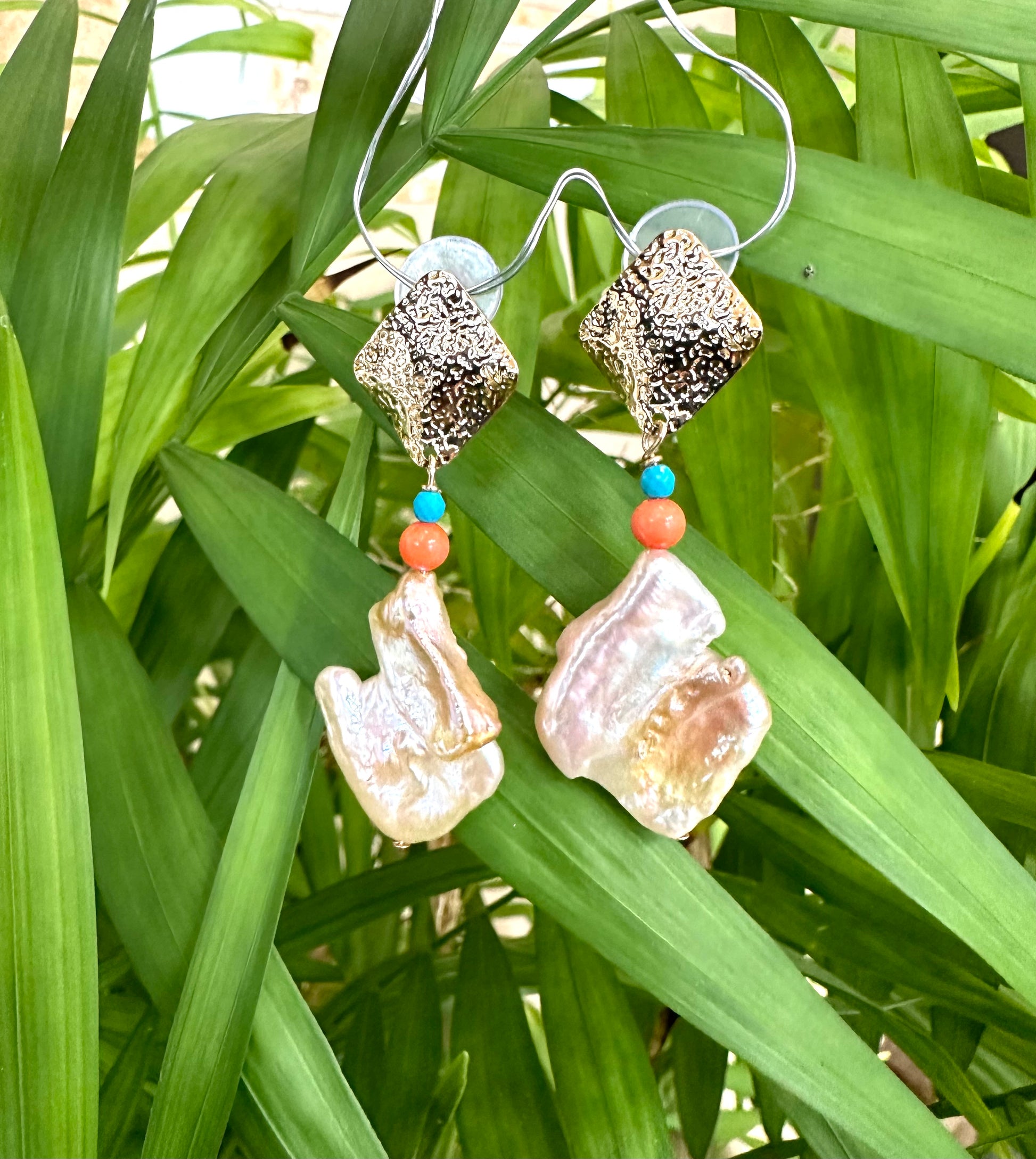 Baroque Pearl Turquoise Coral Earrings featuring bold baroque pearls and vibrant beads, set against lush green foliage.