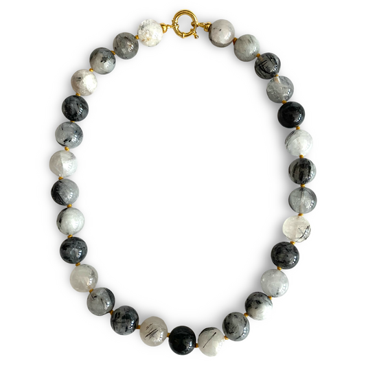 A beaded necklace made of round polished beads in black, white, and gray with natural marbling, separated by small gold spacers and finished with a gold clasp, shown on a plain white background.
