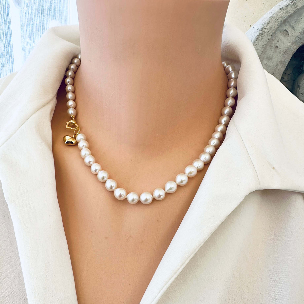 Classic pearl necklace with gold heart charm showcased on a person, highlighting its elegance and timeless beauty.
