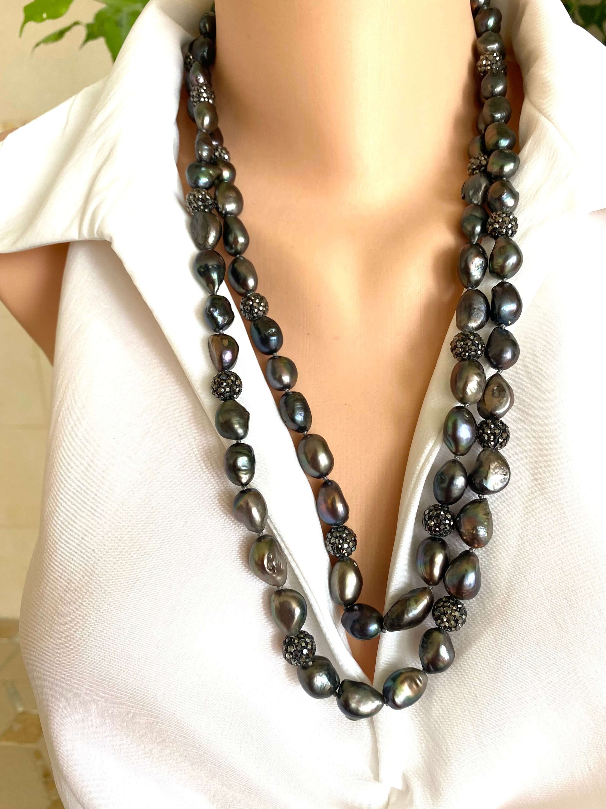 Long black pearl necklace worn by a person in a white outfit.