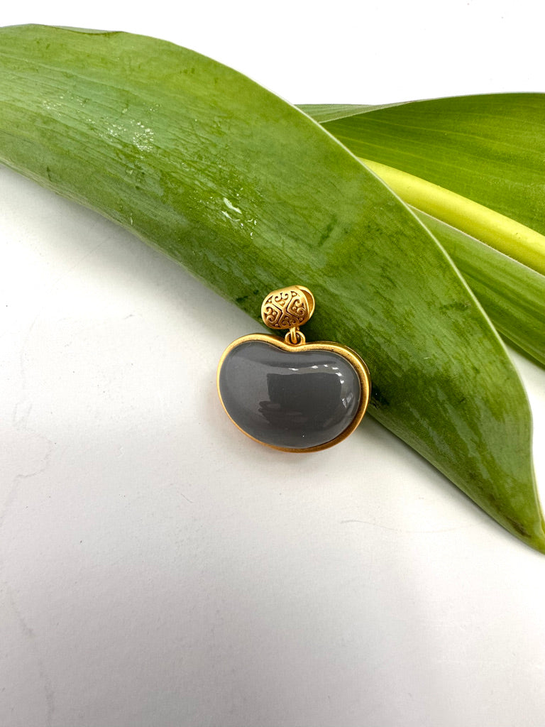 Gold pendant with a gray stone on a white background with green leaves