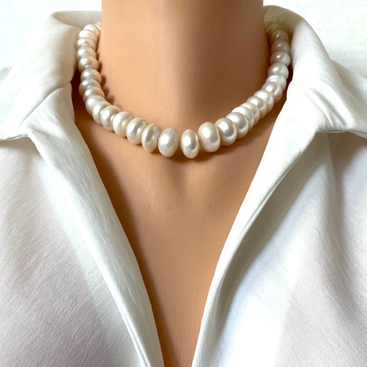 A close-up of a white pearl collar necklace worn on a mannequin or model torso, paired with a white satin blouse.