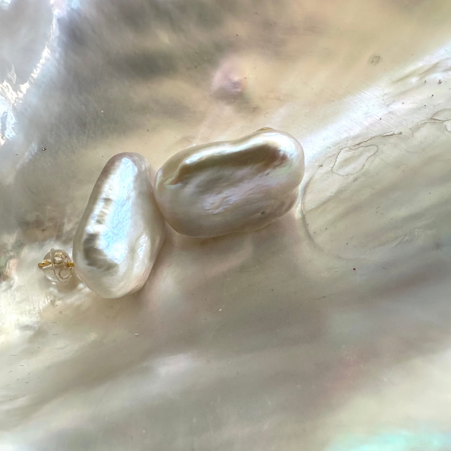 White rectangular baroque pearl stud earrings displayed on white pearl shell, highlighting organic shape and sterling silver posts.