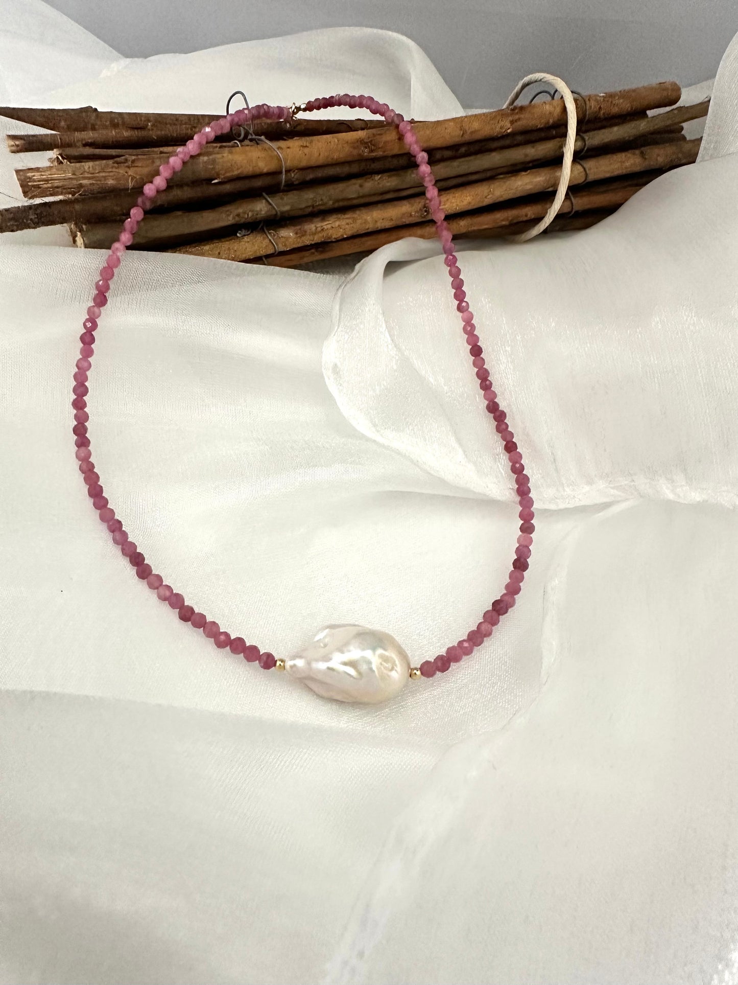 pink tourmaline baroque pearl necklace displayed on white cloth background