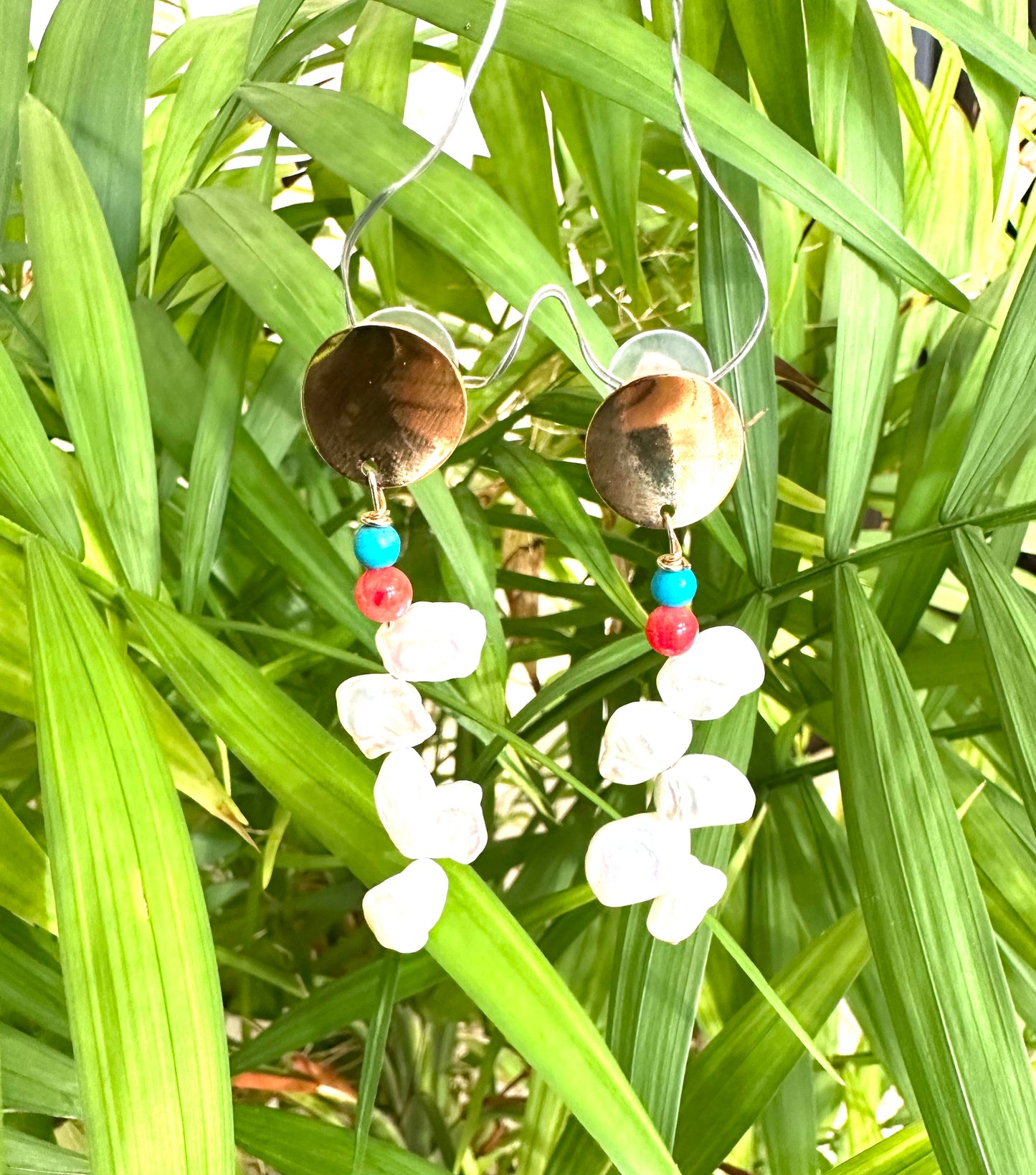 Baroque Keshi Pearl Earrings dangling from green leaves in natural sunlight, showing lustrous freshwater pearls and coral accents