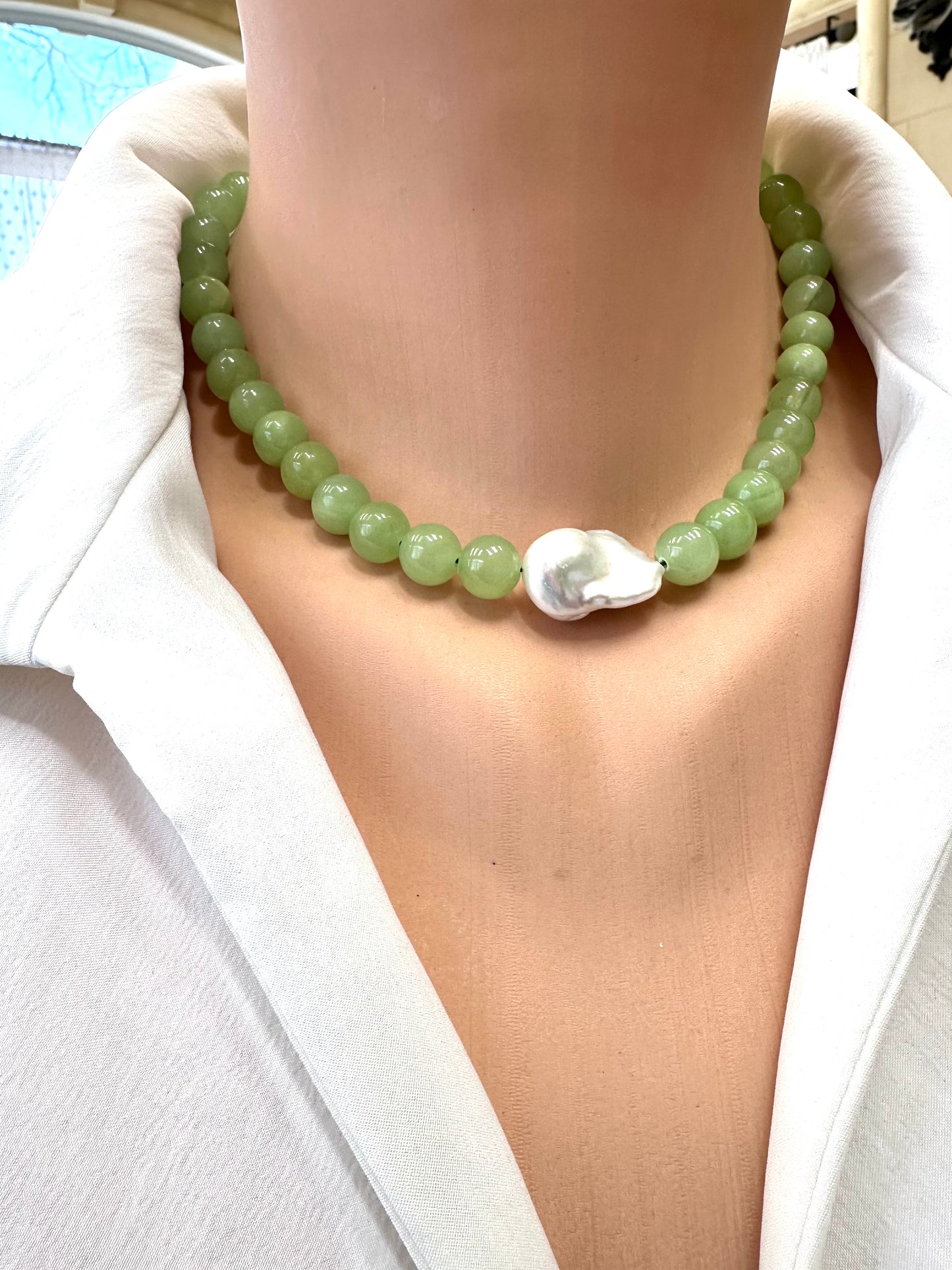 Necklace with green beads and a shell pendant on a white shirt