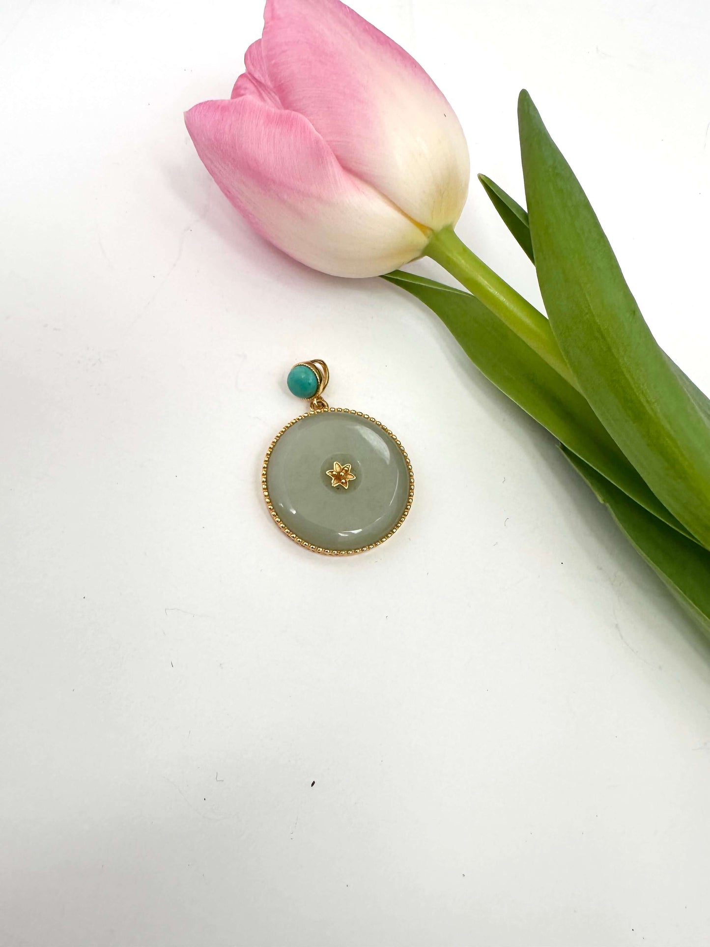 Hotan jade pendant with turquoise accent in gold vermeil beside a pink tulip on a white background.