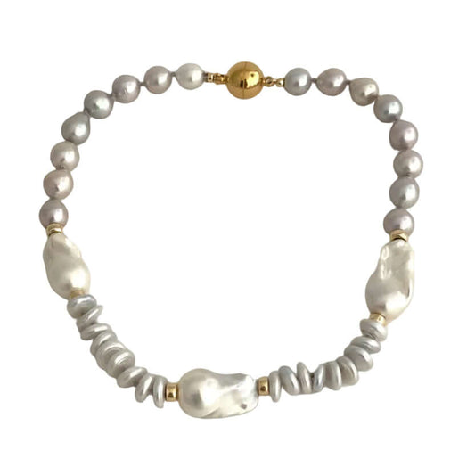 A beaded bracelet featuring a strand of small gray pearls, a few larger white baroque pearls, textured gray beads, and gold spacer accents, displayed on a light beige background.