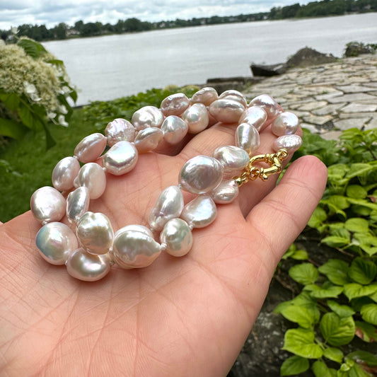 Coin pearl necklace with gold marine clasp held in hand near a lakeside