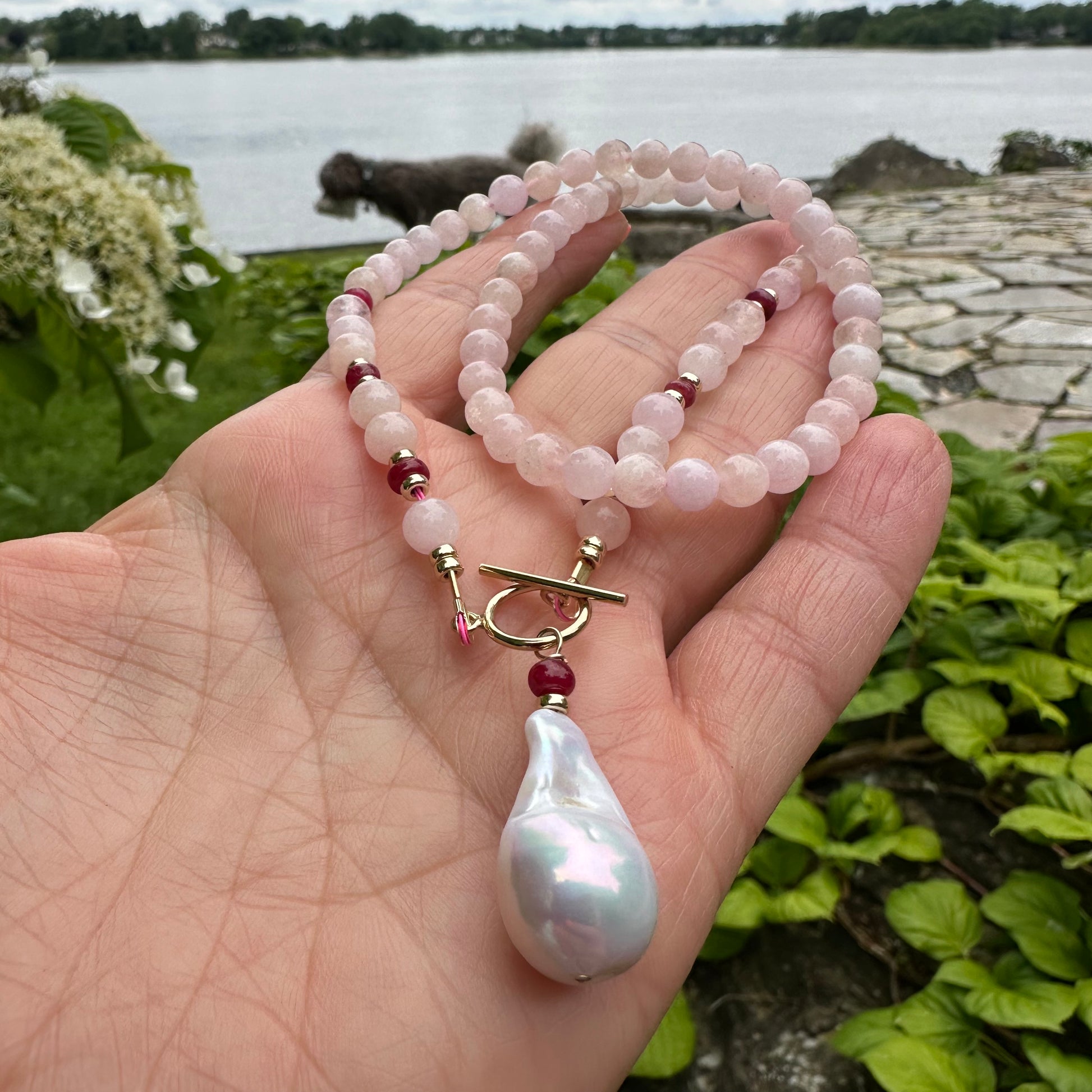 Close-up of morganite necklace with baroque pearl pendant held against greenery