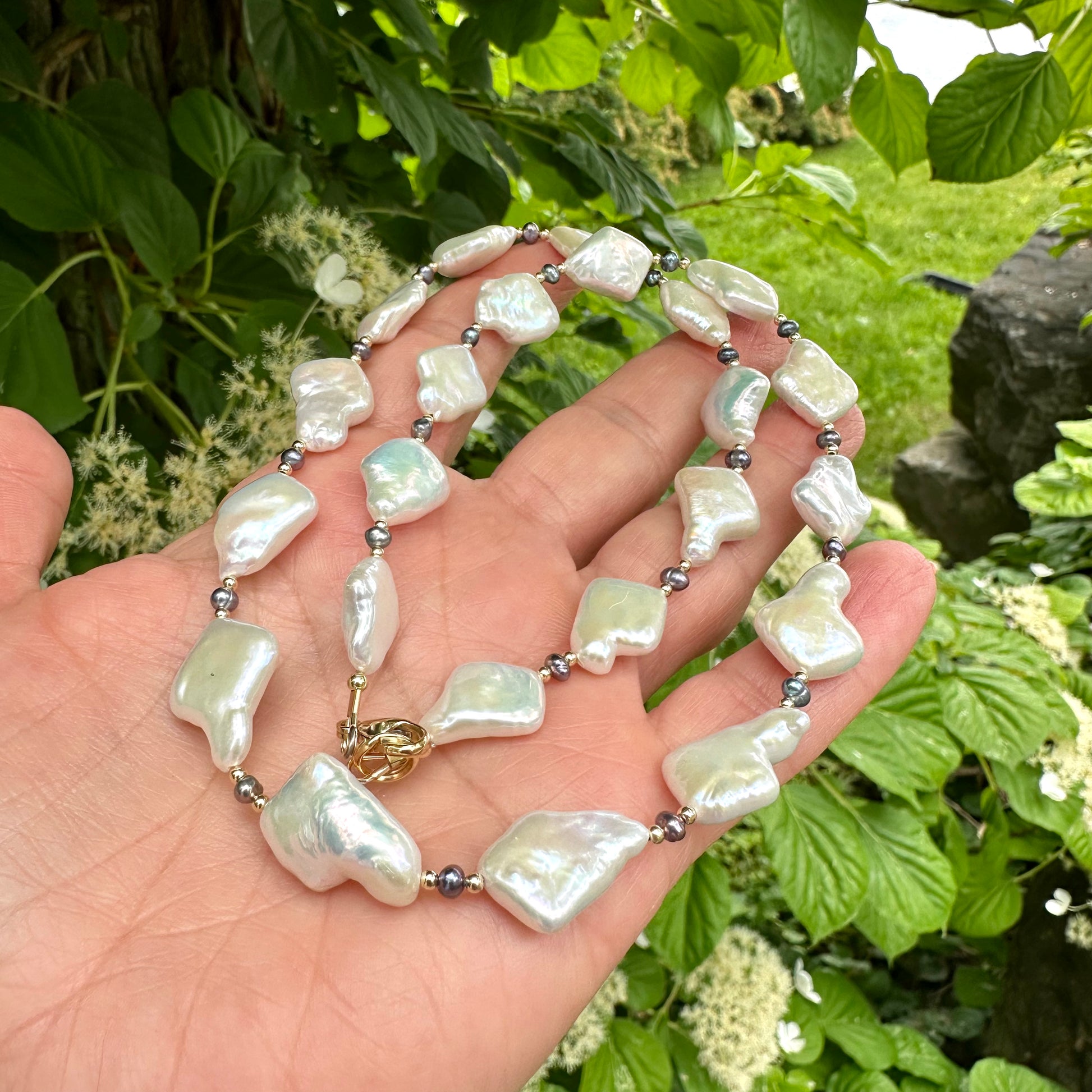 Black and White Pearl Necklace held in hand against green leaves – outdoor close-up