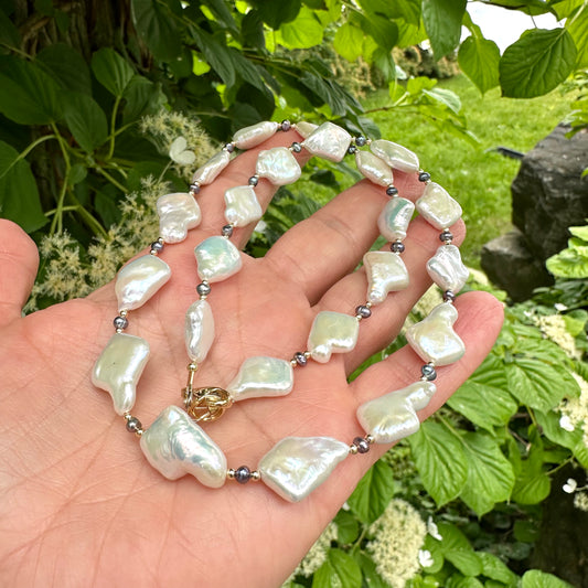 Black and White Pearl Necklace held in hand against green leaves – outdoor close-up