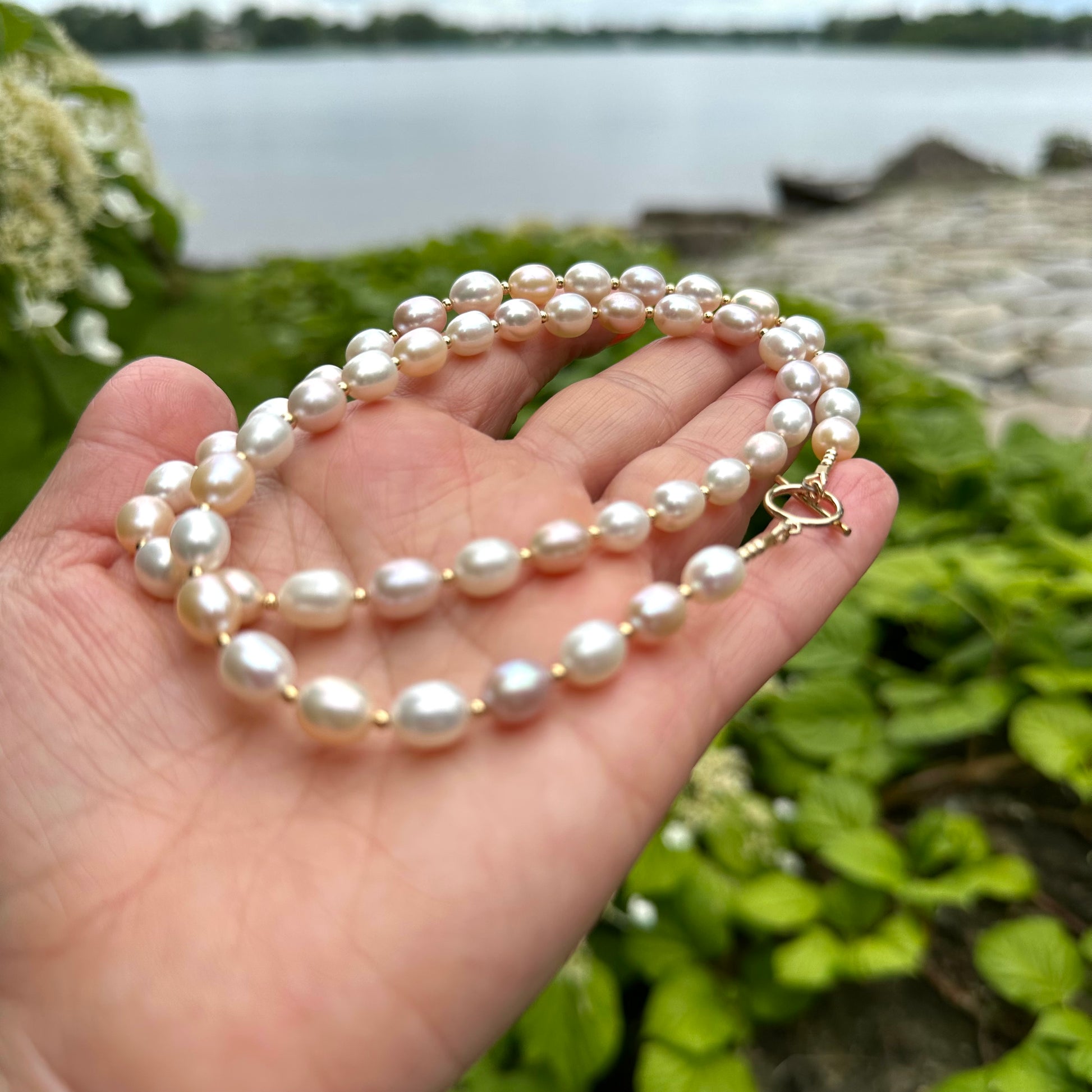 Pastel pearl necklace held in hand against green foliage outdoors