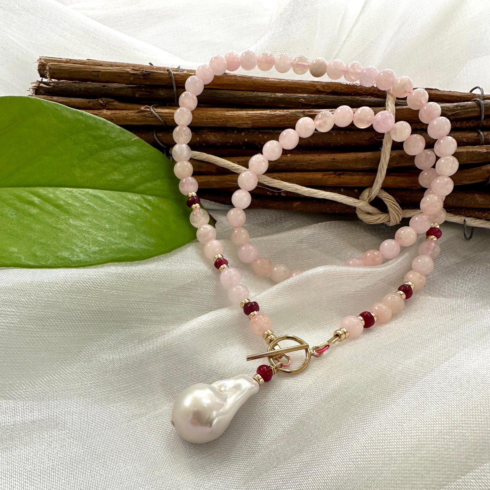 Morganite necklace with ruby accents and baroque pearl displayed on white cloth