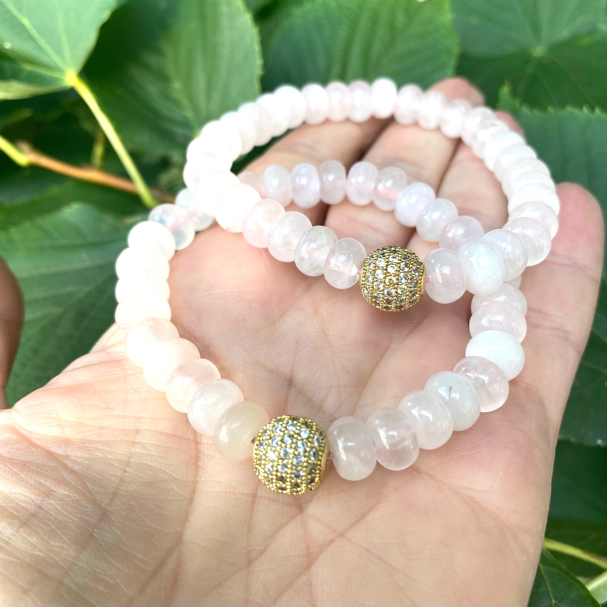 Rose quartz stretch bracelet with gold accent beads shown on a hand against green foliage.