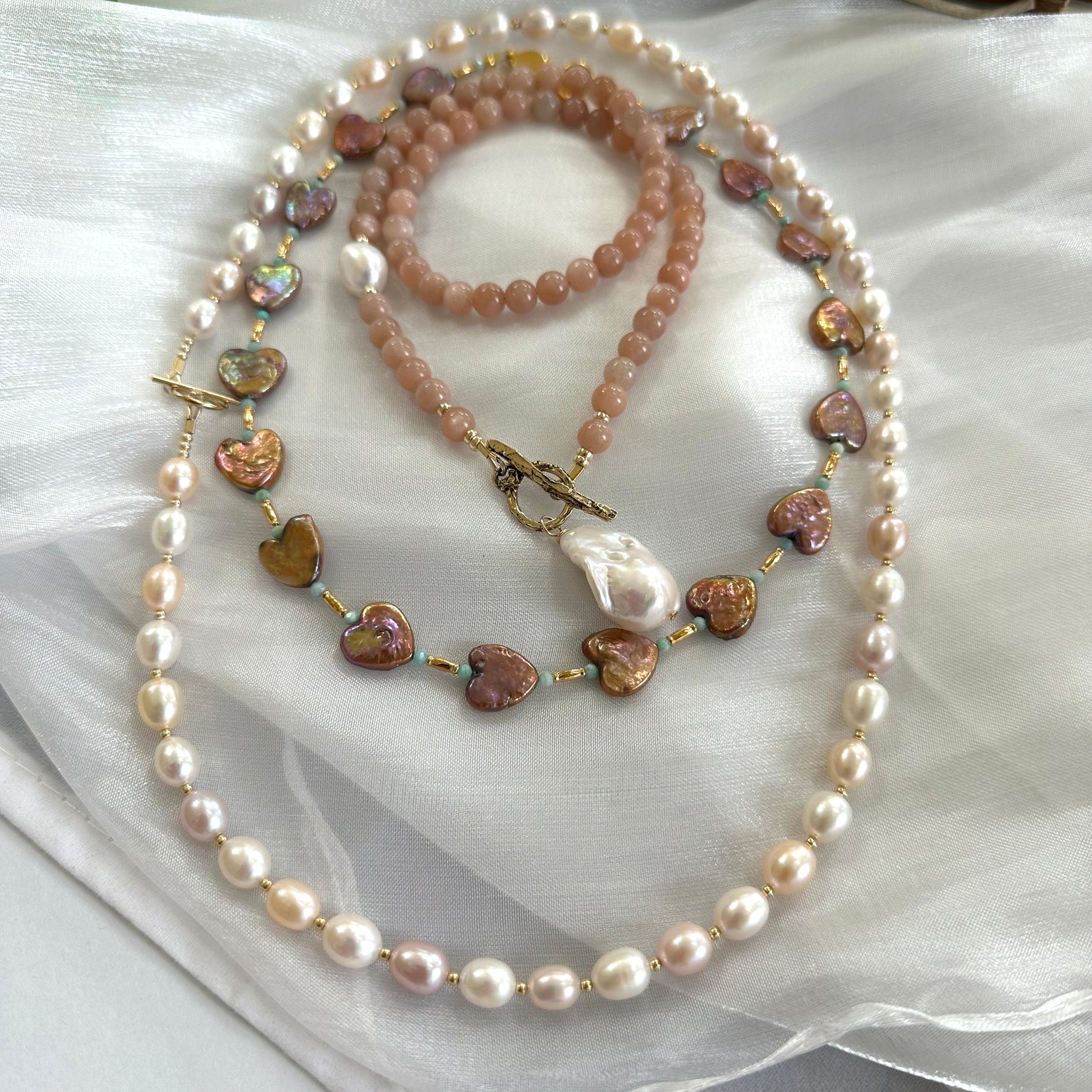 Sunstone necklace placed alongside two pearl necklaces on white cloth