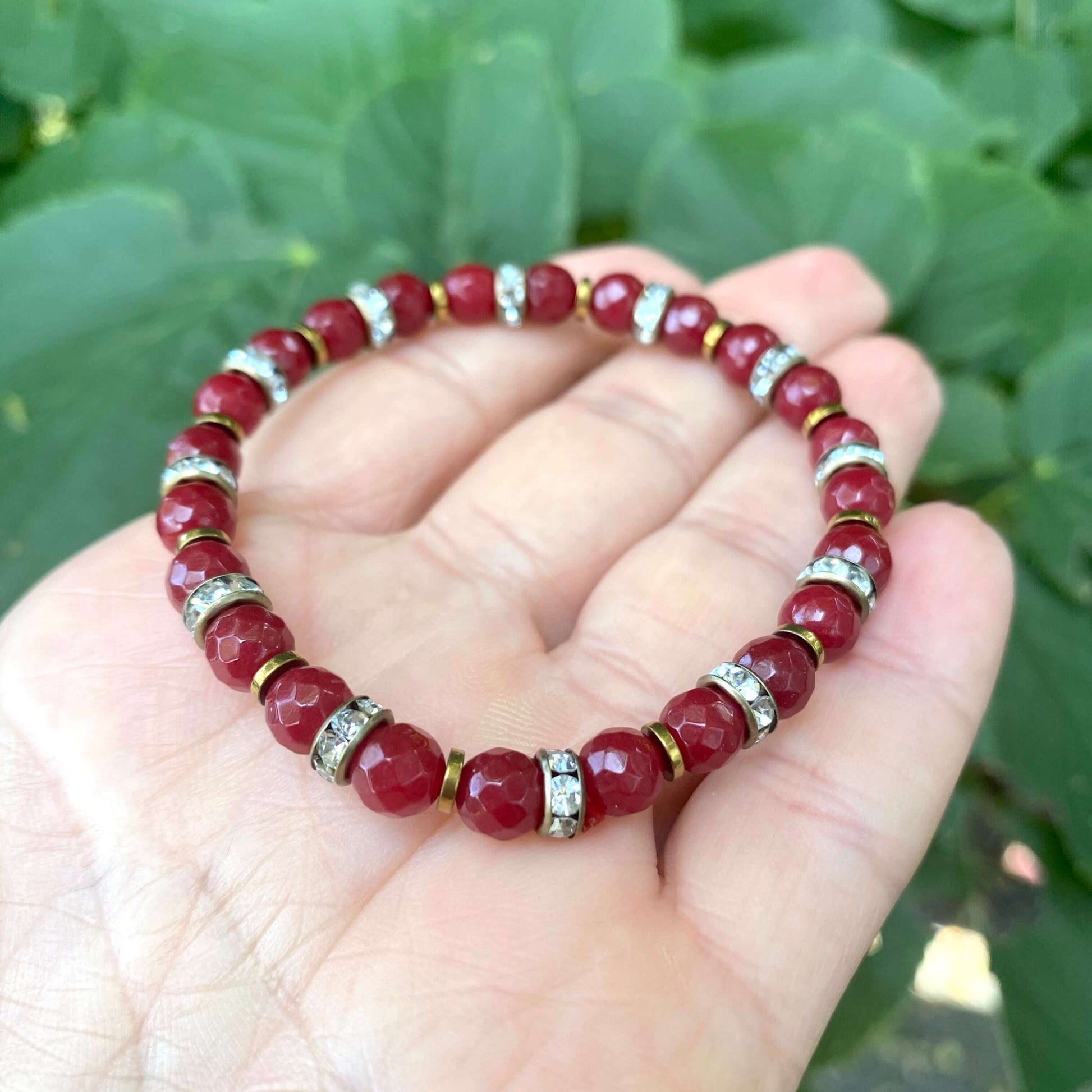 Pale blue deep red stretchy bracelet held in hand highlighting deep red gemstone beads
