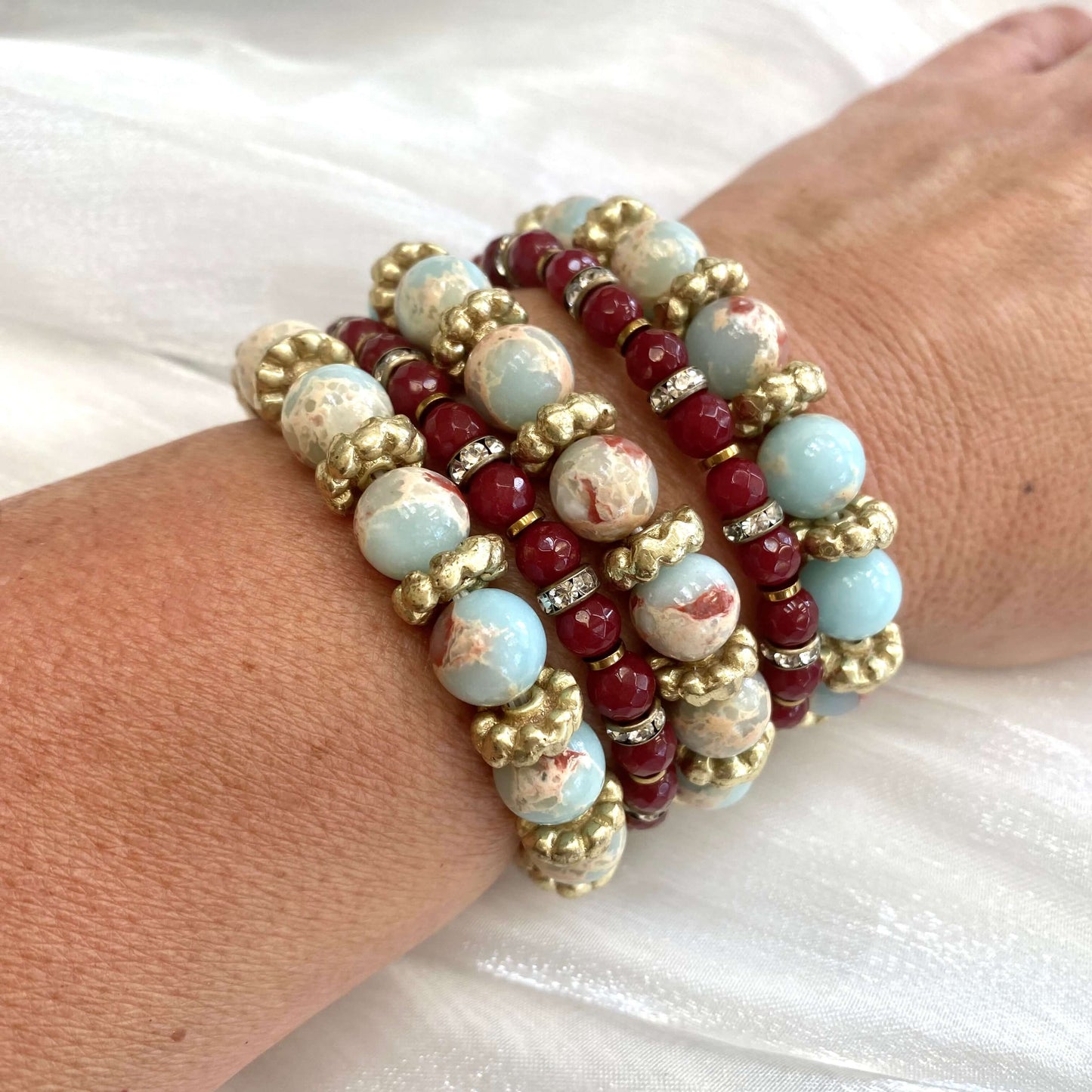 Pale blue deep red stretchy bracelet stack styled on wrist with brass and pearl accents