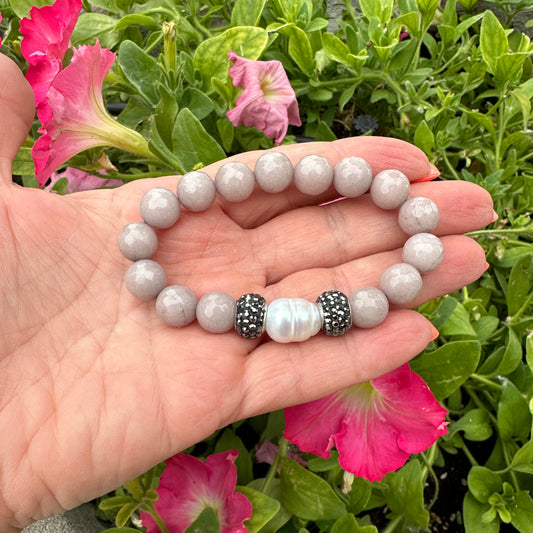 Pink jade pearl bracelet held in hand against green foliage