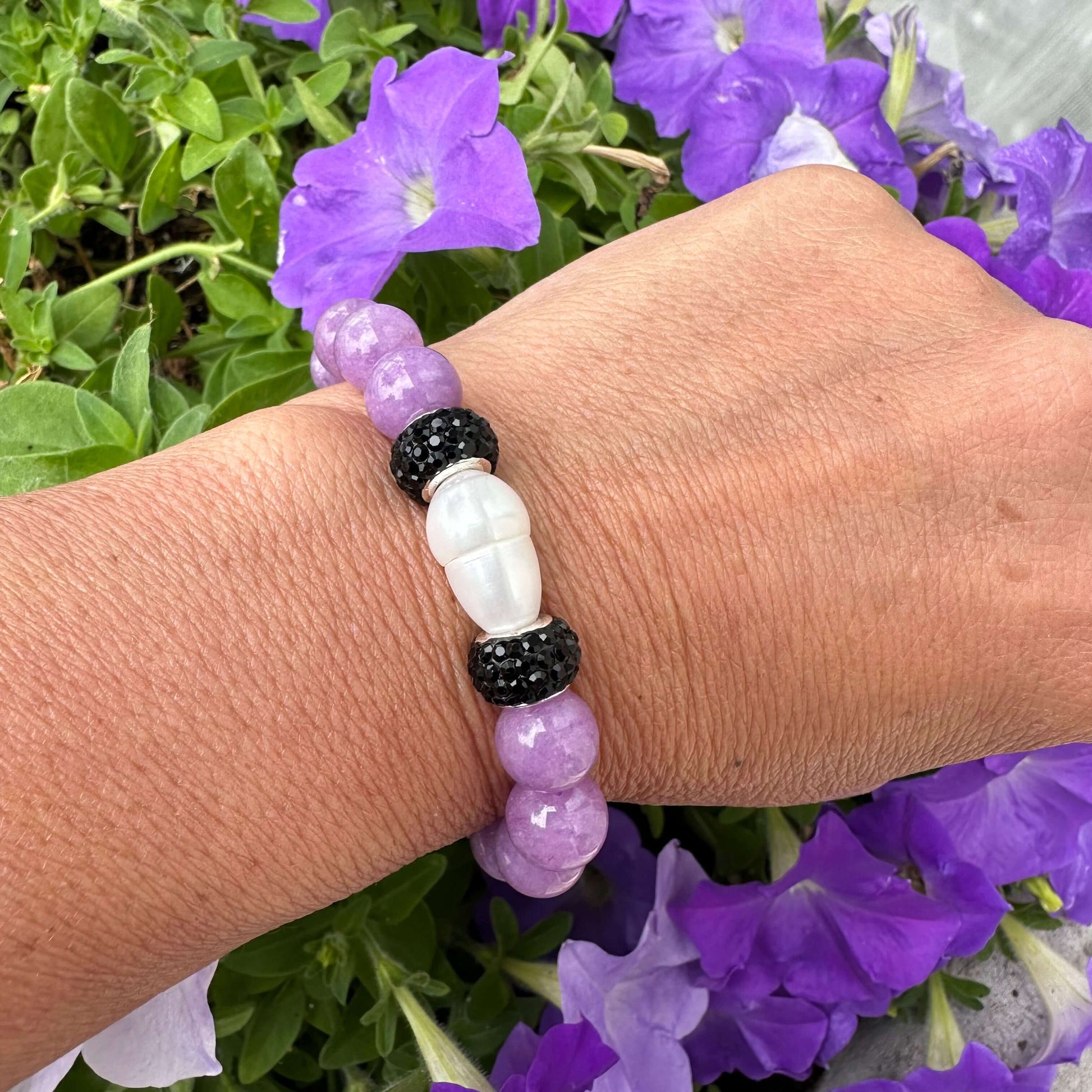 Lavender jade bracelet with pearl worn on a woman’s wrist beside flowers